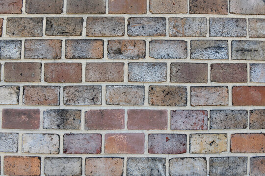 A full-frame view of a weathered brick wall featuring varied tones of red, grey, and brown bricks set in light mortar from the historic fortress walls in Prague.