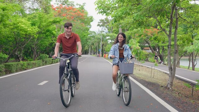 Young Caucasian couple dating and biking together on a road in the park. 