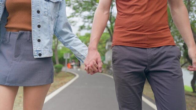 Close up of young couple holding hand while walking through beautiful park. 