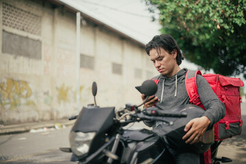 Delivery courier checking phone while holding motorcycle helmet outdoors. Courier reading...
