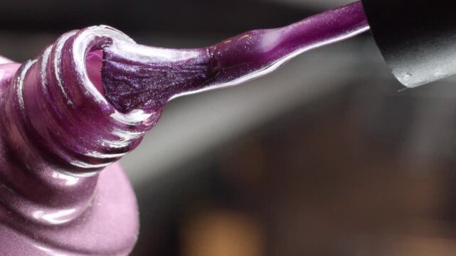Macro close up of glossy purple nail polish coating a brush applicator, highlighting the thick lacquer texture and reflective surface during nail care application