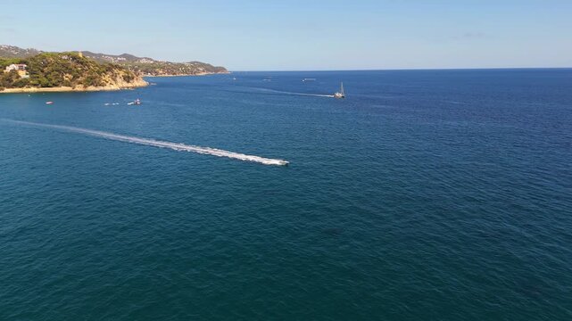 An aerial drone view of a motorboat riding high-speed waves near the town of Lloret de Mar on the Costa Brava, Spain, on a sunny summer day.
