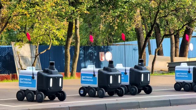 Autonomous courier robots for contactless delivery fill a close static frame with six wheels sensor towers glowing lights and red safety flags while the machines wait by a city road