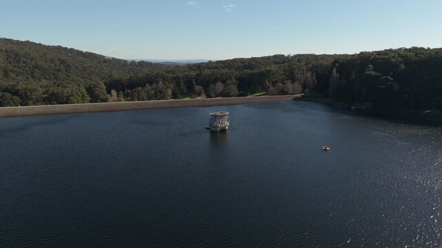 Aerial shot slowly flies backward over a tranquil water reservoir on a sunny day
