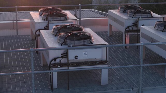 Industrial air conditioning units with spinning fans on a rooftop during sunset