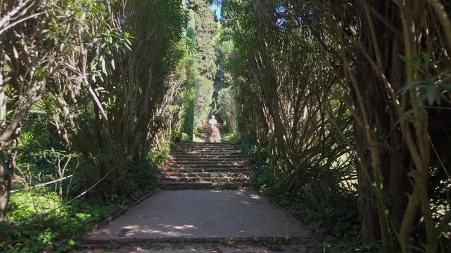 Steps on the shady alleys of Santa Clotilde Park in Lloret de Mar, Costa Brava, Spain - paths among green trees and bushes, statues