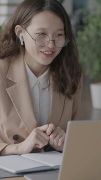 Asian businesswoman making online video call with laptop and wireless earphones speaking discussing business in office. Communication and job concept.