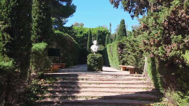 Steps on the shady alleys of Santa Clotilde Park in Lloret de Mar, Costa Brava, Spain - paths among green trees and bushes, statues