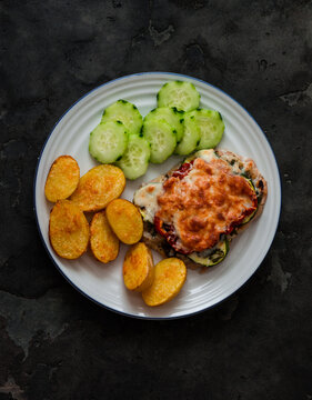 Baked meat chop with zucchini, tomato, mozzarella, baby potatoes, cucumber - a delicious balanced lunch on a dark background, top view