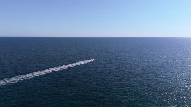 An aerial drone view of a motorboat riding high-speed waves near the town of Lloret de Mar on the Costa Brava, Spain, on a sunny summer day.