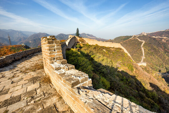 A section of ancient stone Great Wall winds along mountain ridges under a clear blue sky, showing historic fortification architecture.