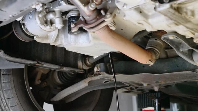 Close-up view of used engine oil flowing from the underside of a raised vehicle during routine oil change service