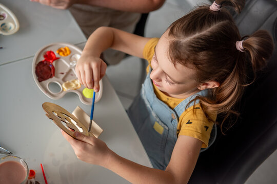 Young girl paint wooden mask at craft table