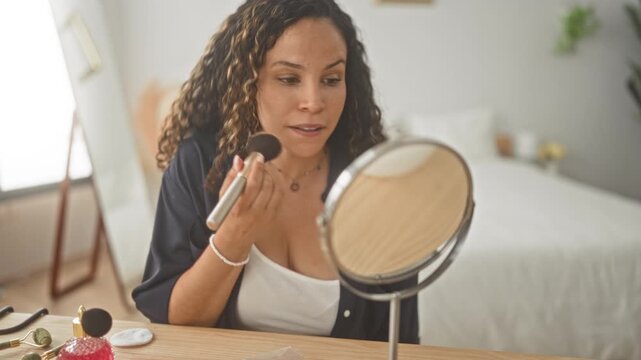 Woman applying makeup with a powder brush to her cheek at a vanity mirror in a studio bedroom, focused on reflection and routine; self care calm.