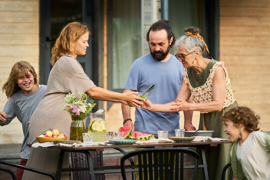 Caucasian family including senior woman, middle aged parents, and children gathering around outdoor table for lunch. Useful for multigenerational living and healthy nutrition campaigns