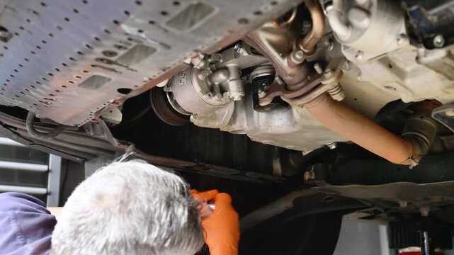Mechanic using a socket wrench to loosen the oil drain plug underneath a raised vehicle during an oil change service