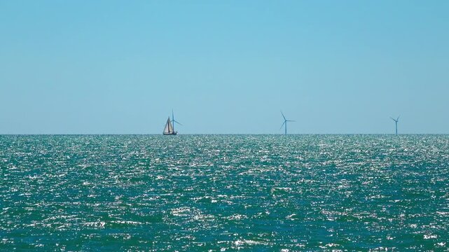 Boat sails across the water near wind turbines. Valras, France .