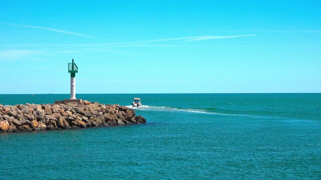 Boat sails past green light on rocky jetty. Valras, France .