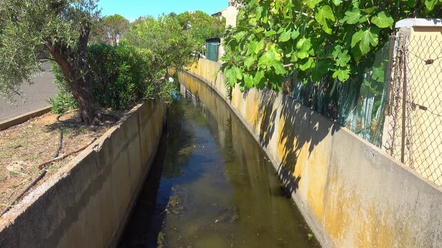 Water flows slowly in the channel beside a path. Valras, France .