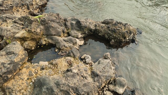 High angle view of natural rock tide pools formed on a rugged rocky riverbank along a flowing freshwater stream