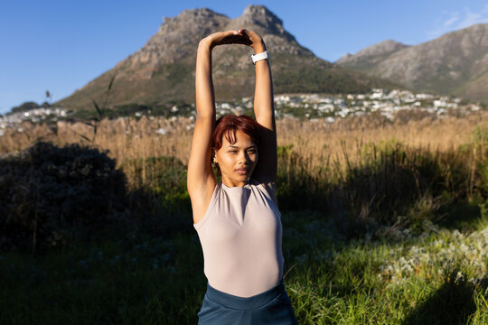 African American adult woman stretching arms in marsh near town with white smartwatch and tank top