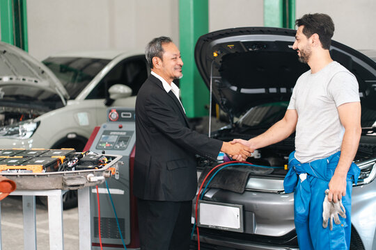 Ev car battery cells service Business handshake between mechanic and customer beside vehicle in auto repair shop
