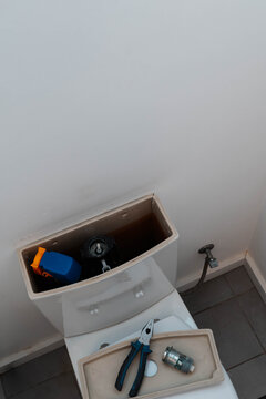 Cracked ceramic toilet cistern stands open with pliers and a worn fill valve resting on the removed lid. Bathroom plumbing repair and home leak troubleshooting by a handyman.