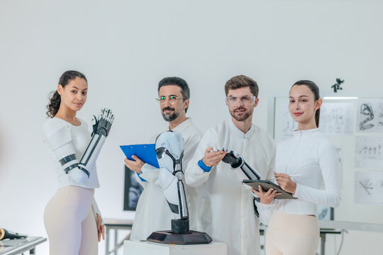 Four robotics engineers examining bionic arm and robotic hand in white research laboratory