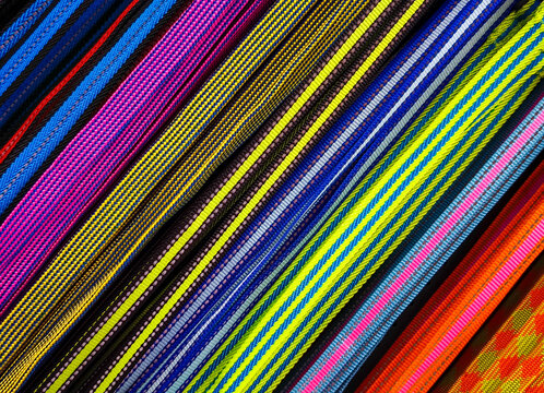 Close-up of colorful, woven fabric straps, nylon webbing, or elastic bands arranged in parallel diagonal lines. Various colorful, textured woven straps
