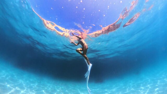 Woman swimming underwater with long white fins in azure sea. Wide tracking shot.