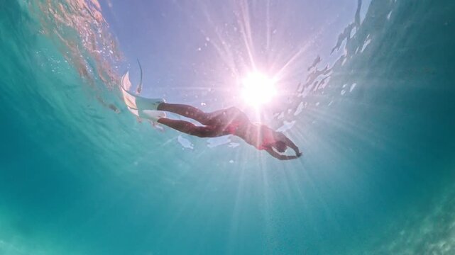 Freediver gliding through sunny turquoise ocean waters. Underwater wide angle shot.