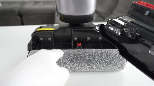 Gloved hands fitting plastic components of a vacuum cleaner head assembly on a table surface during maintenance
