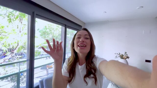 Happy woman taking a selfie video, showing off her new apartment keys while on a video call with friends or family, celebrating her achievement and sharing her excitement with her loved ones