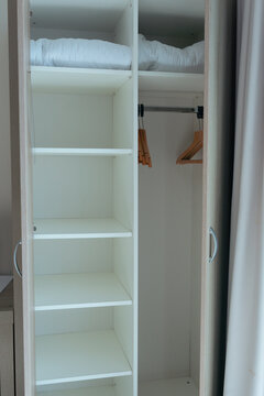open white wardrobe closet empty shelves wooden hangers folded blankets hotel room interior bedroom furniture concept of travel, hospitality, interior design