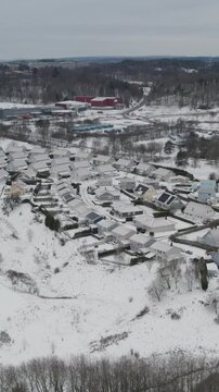 Aerial drone view of a villa area with snow covered homes, roads and gardens, surrounded by wooded hills and industrial buildings during winter in Storas, Angered, Gothenburg, Sweden.