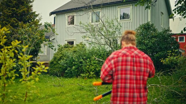 A man uses a reciprocating saw to cut tree branches in a rural Norwegian outdoor setting