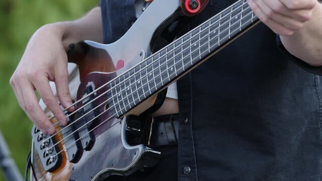 Close up fingers: Outdoor musician plays 5-string electric bass at gig