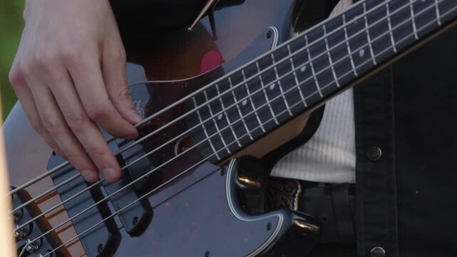 Closeup bassist's hand as he plays electric bass on outdoor stage