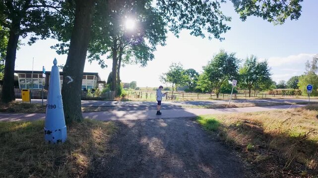 Young male runner stopping mid-run on asphalt bicycle lane to check his phone in the countryside with the border landmark of BE-NL.