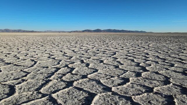 Hexagonal salt crust patterns cover the flat surface of Salinas Grandes with distant mountains under a clear blue sky, useful for climate, geology, or lithium mining stories.