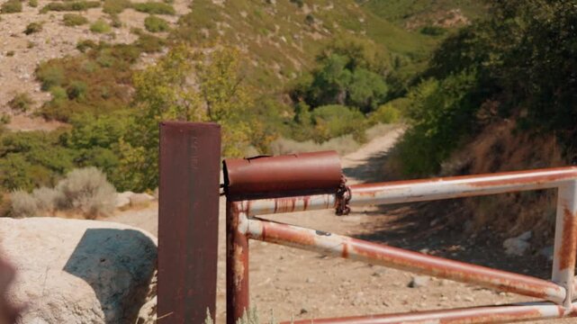 Left to right glide moves past a foreground post to reveal a rusty gate on a trail.