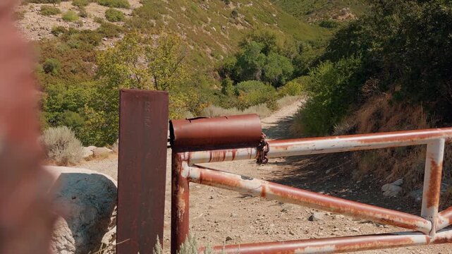 Right to left camera glide keeps a rusted gate in focus on a mountain trail.