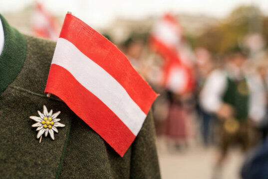 Austrian flag and edelweiss brooch on traditional woolen jacket during a parade celebration.