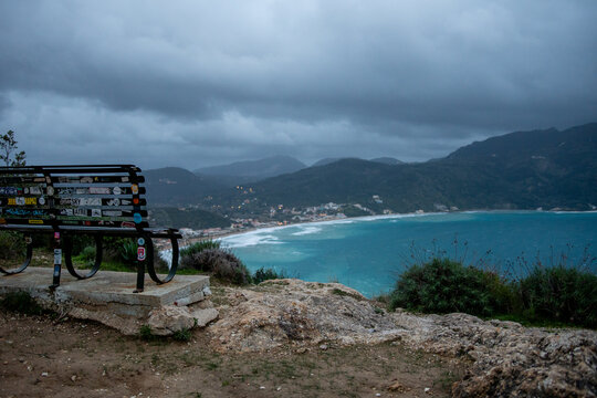 Close Up of Metal Bench Covered in Stickers at Afionas Viewpoint Corfu Greece with Blurred Background of Stormy Sea and Coastline