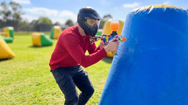 outdoor adventure sports, a focused player in protective gear aims a gellyball blaster in a vibrant arena