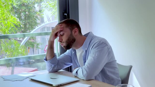 Stressed and disappointed young businessman closing his laptop in anger after receiving bad news or facing a computer failure, feeling exhausted and defeated in his modern office