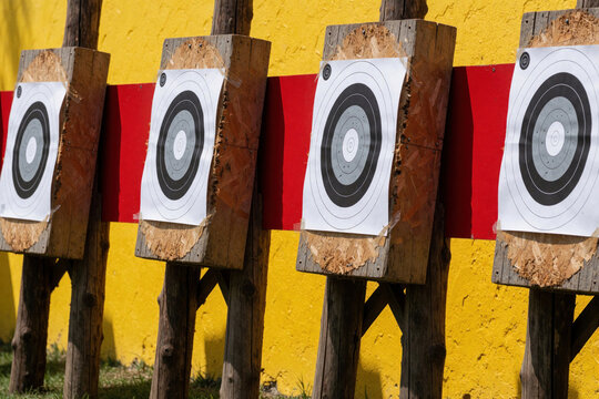 Row of shooting targets attached to wooden posts, set against a bright yellow wall with a red stripe. These targets are for practice and competition use in outdoor ranges.