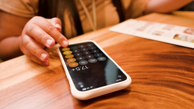 Woman Using Calculator on Smartphone at Restaurant Table