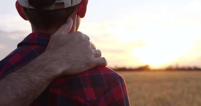 Close-up shows father hand resting on son shoulder while walking together at sunset. Genuine family moment symbolizes trust, encouragement, emotional connection and unconditional support through life.