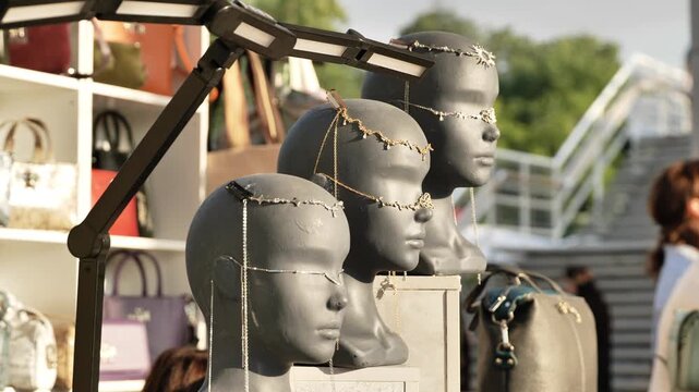 Mannequin heads displaying fashion jewelry and headpieces at an outdoor market stall